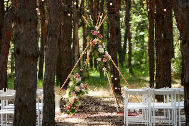 Belle décoration d'arc de tipi bohème sur le lieu de la cérémonie de mariage en plein air dans la forêt de pins avec des cônes