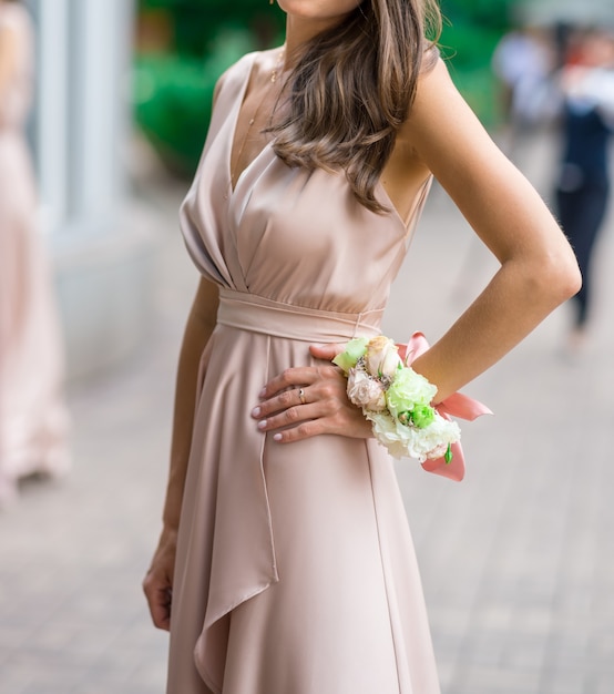 Belle demoiselle d'honneur dans une robe en soie avec une fleur à la boutonnière sur sa main contre un jardin verdoyant