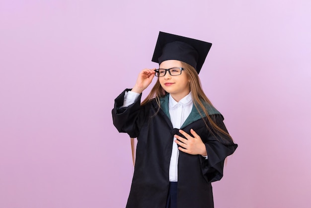 Une belle diplômée vêtue d'une robe de cérémonie de remise des diplômes noire regarde pensivement au loin et tient ses lunettes. fond violet isolé.