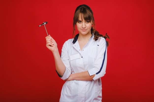 Une belle doctoresse tient un marteau réflexe et sourit à la caméra isolée sur fond rouge
