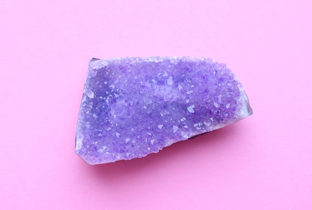 Belle druse d'améthyste minérale violette naturelle sur un mur rose. Grands cristaux de pierres précieuses.