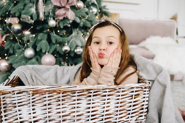 Belle écolière caucasienne assise dans un panier près de l'arbre de Noël décoré