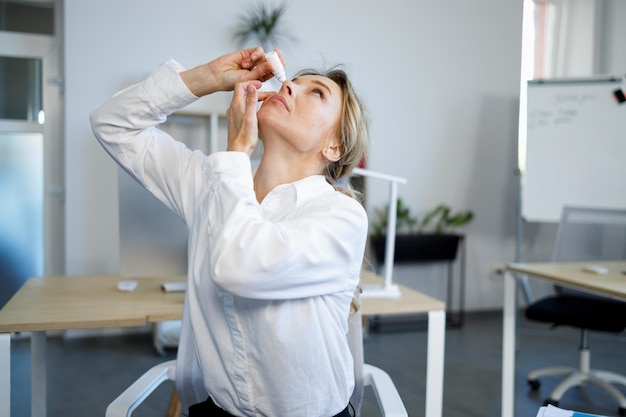 Une belle employée de bureau ressent une fatigue oculaire et applique des gouttes pour les yeux