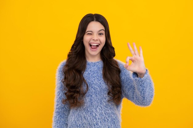 Belle enfant fille faisant signe ok sur fond jaune Portrait d'un enfant souriant montrant le symbole des mains confiantes