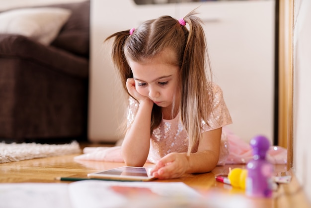 Belle enfant fille joue avec une tablette sur le sol.