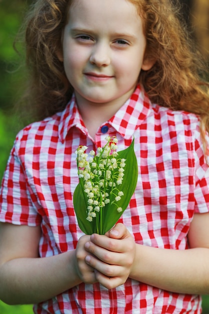 Belle enfant avec le muguet dans la forêt de printemps.