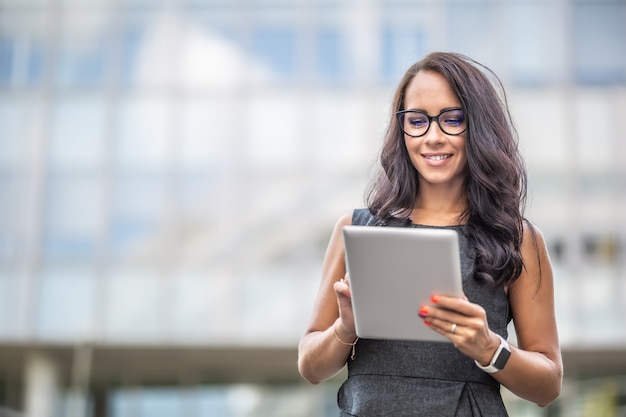 Une belle entrepreneure lit à partir d'une tablette en souriant, marchant à l'extérieur.