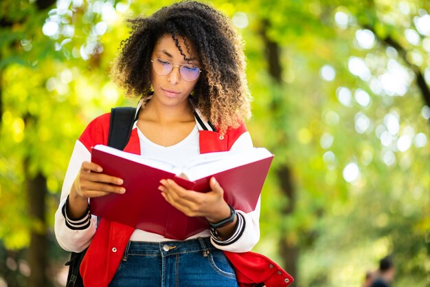 Photo une belle étudiante africaine lisant un livre sur un banc dans un parc.