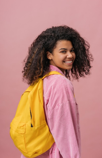 Belle étudiante afro-américaine avec sac à dos regardant la caméra isolée sur fond rose