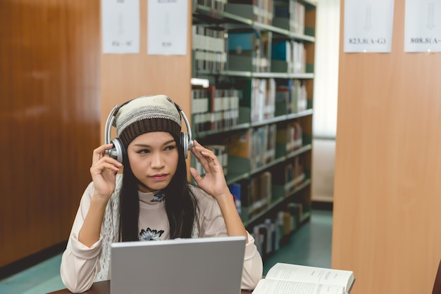 Belle étudiante asiatique écouter une chanson avec un ordinateur portable dans la bibliothèque