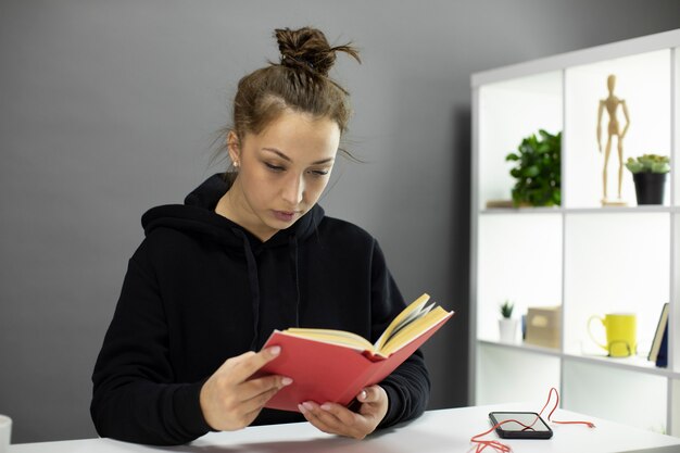 Belle étudiante assise à la maison, lit la littérature pédagogique, l'auto-isolement