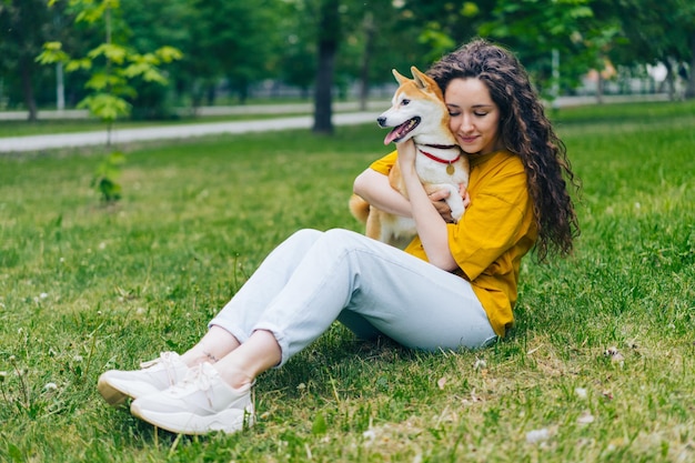 Belle étudiante étreignant un chiot shiba inu sur une pelouse verte dans le parc