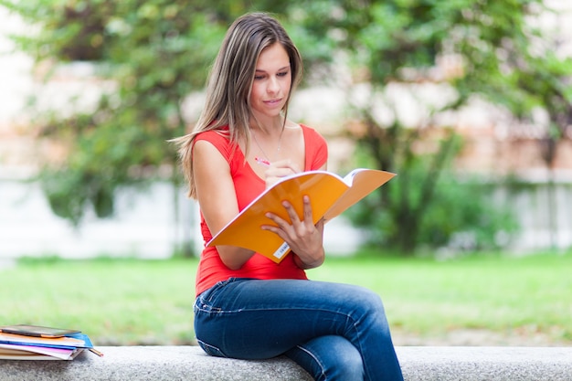 Belle étudiante lisant un livre sur un banc dans un parc