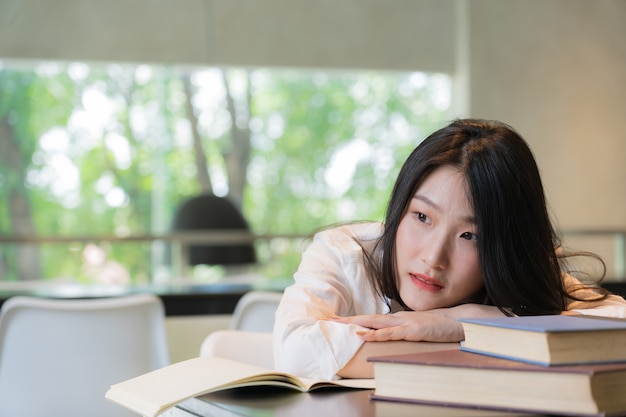 Photo belle étudiante portant une chemise blanche au repos tout en lisant des livres sur la table dans la bibliothèque