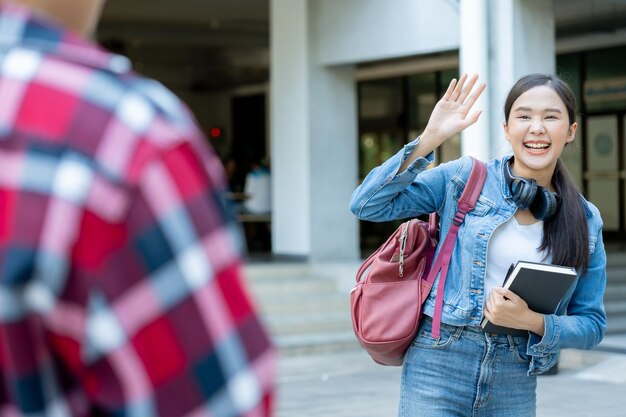 Photo belle étudiante avec sac à dos et livres en plein air salue des amis fille souriante heureuse portant beaucoup de livres sur le campus universitaire portrait féminin sur l'éducation universitaire internationale en asie