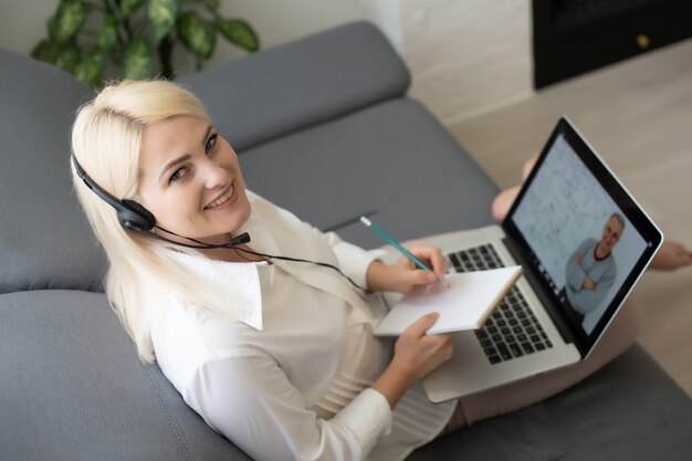 Photo belle étudiante souriante utilisant le service d'éducation en ligne. jeune femme regardant dans un écran d'ordinateur portable en regardant un cours de formation et en l'écoutant avec des écouteurs. concept de technologie d'étude moderne