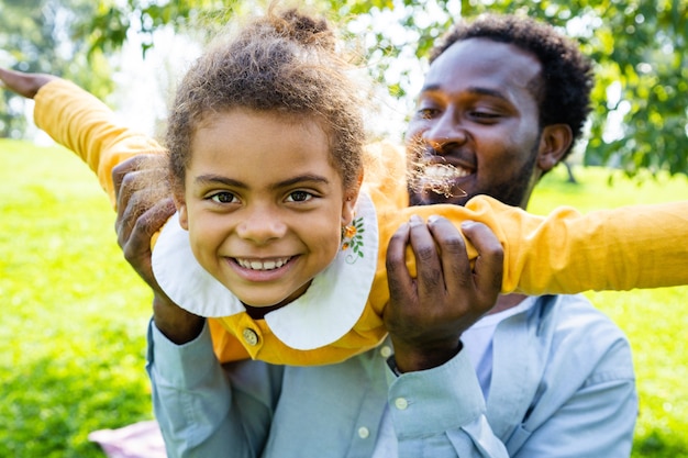 Belle famille afro-américaine heureuse au parc - Famille noire s'amusant à l'extérieur, papa jouant avec sa jolie fille