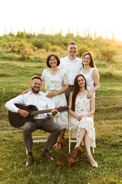 Belle famille au coucher du soleil du jour. grande famille heureuse. passe-temps dans le cercle des parents. père joue de la guitare et heureuse mère et filles avec son fils se tiennent à proximité.