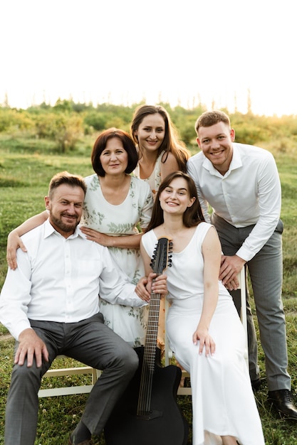 Belle famille au coucher du soleil du jour. grande famille heureuse. passe-temps dans le cercle des parents. père joue de la guitare et heureuse mère et filles avec son fils se tiennent à proximité.