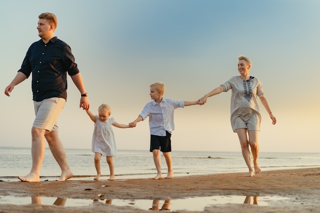 Belle famille caucasienne s'amusant à courir dans la mer au coucher du soleilVacances d'été avec des enfants