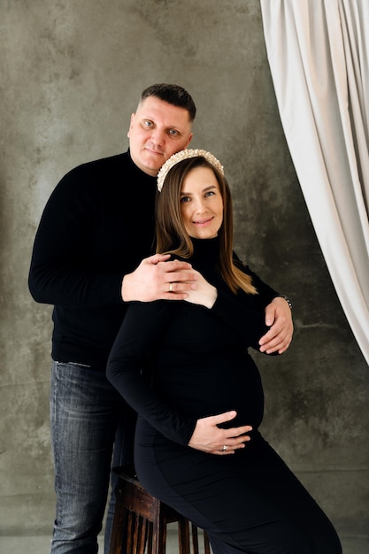 Belle famille enceinte. un homme embrasse et embrasse doucement une jeune et belle femme enceinte. fille enceinte dans une robe moulante noire. heureux futurs parents.