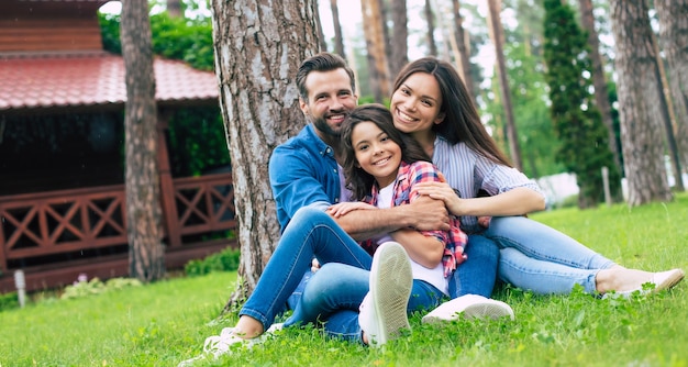 Belle famille heureuse assis ensemble sur l'herbe et s'embrassant