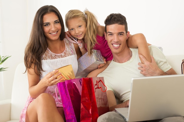 Belle famille heureuse assise à la maison avec un ordinateur portable et des sacs à provisions.
