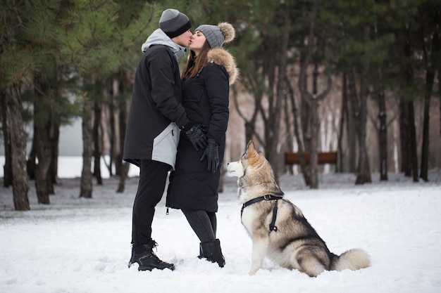 Belle famille, un homme et une fille dans la forêt d'hiver avec chien. Jouez avec le chien husky sibérien.