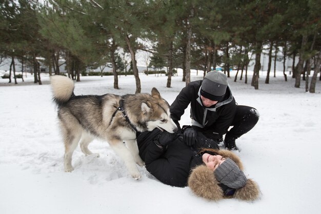 Belle famille, un homme et une fille dans la forêt d'hiver avec chien. Jouez avec le chien husky sibérien.
