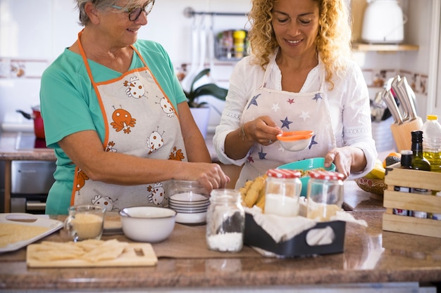 Belle famille à la maison cuisinant et s'amusant ensemble - grand-mère montrant comment cuisiner des biscuits et du poisson - mode de vie intérieur - femme caucasienne et femme mûre s'amusent