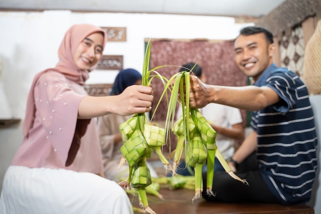 Belle famille musulmane et ami faisant un gâteau de riz ketupat à la maison à l'aide de feuilles de palmier pour la tradition de l'Aïd fitr moubarak