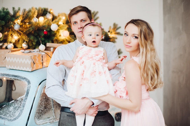 Belle famille posant ensemble près de la voiture de Noël rétro bleue.