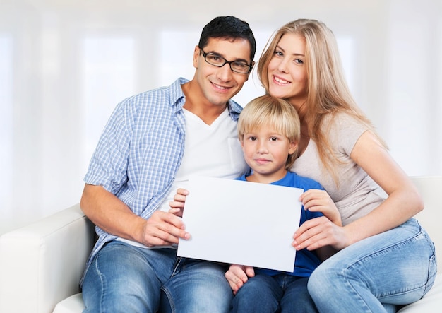 Belle famille souriante avec une affiche assise sur un canapé en arrière-plan