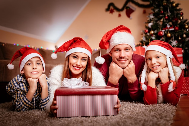 Belle famille souriante avec bonnet de Noel à Noël à la maison. Ils regardent la caméra.