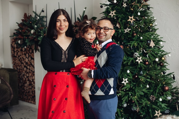 Belle famille de trois poses pour la caméra sur le fond d'arbre de Noël