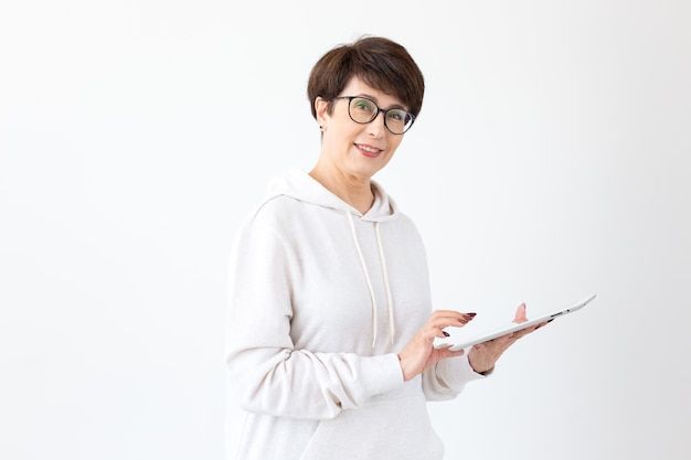 Belle femme de 50 ans aux cheveux courts tenant la tablette sur le mur blanc.