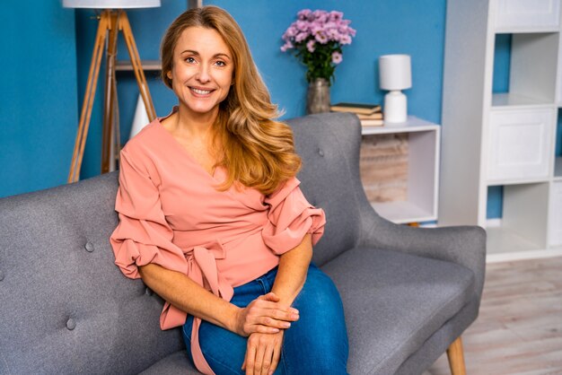 Belle femme adulte assise seule à la maison et regardant la caméra en souriant