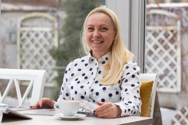 Belle femme adulte aux cheveux blonds travaille dans un café avec un intérieur blanc