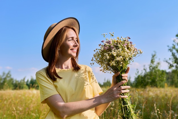 Belle femme adulte heureuse avec bouquet de fleurs sauvages sur la prairie d'été