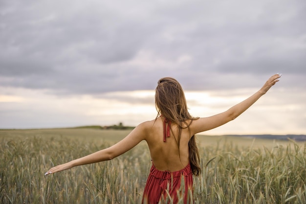 Belle femme adulte portant une robe rouge avec un dos nu dans un champ de blé