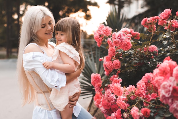 Belle femme adulte tenant une petite fille posant sur des fleurs roses en fleurs