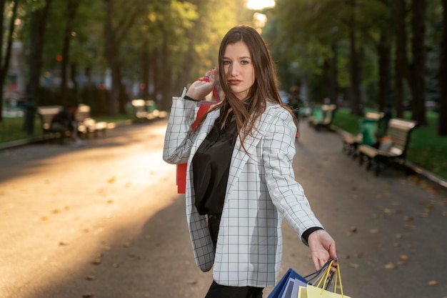 Belle femme d'affaires après le shopping se promène dans un parc ensoleillé Femme heureuse réussie avec des sacs à provisions colorés