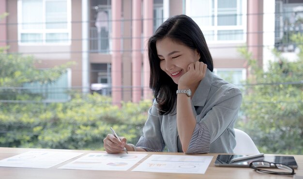 Une belle femme d'affaires asiatique analyse des graphiques à l'aide d'une calculatrice pour ordinateur portable au bureau