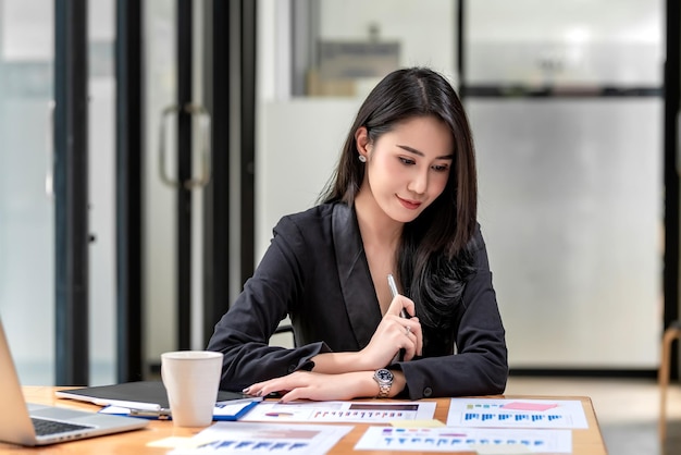 Belle femme d'affaires asiatique assise au bureau avec des papiers graphiques au bureau vérifiant les statistiques de revenu.