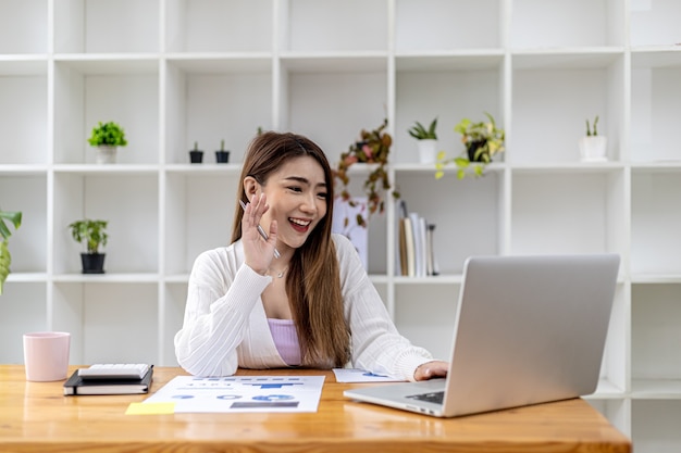 Belle femme d'affaires asiatique assise dans son bureau privé, elle parle à son partenaire par appel vidéo sur son ordinateur portable, c'est une femme cadre d'une start-up. Concept de gestion financière