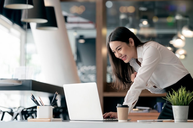 Belle femme d'affaires asiatique célèbre tout en utilisant un ordinateur portable au bureau et en montrant son plaisir.