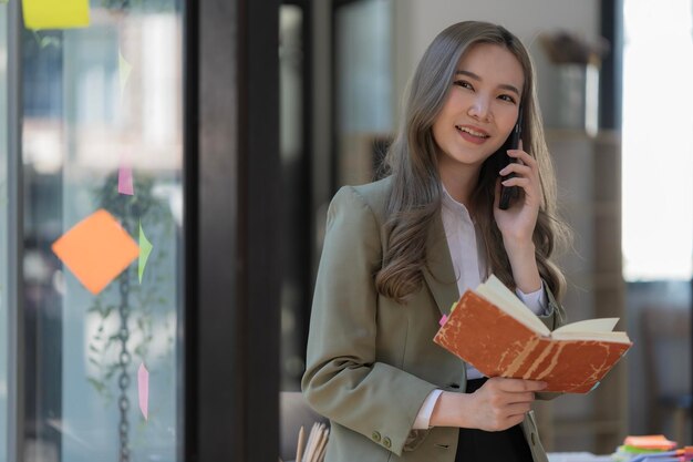 Une belle femme d'affaires asiatique se tient debout et parle au téléphone dans le bureau.