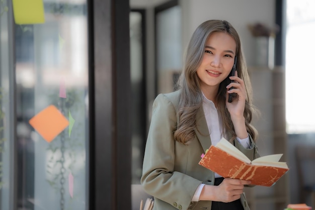 Une belle femme d'affaires asiatique se tient et parle au téléphone dans le bureau et regarde la caméra