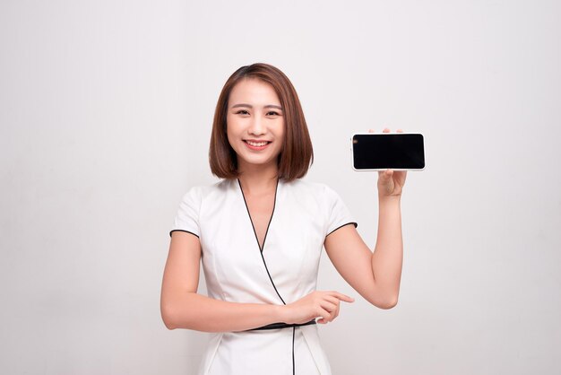 Belle femme d'affaires asiatique tenant et montrant un téléphone portable blanc avec un écran noir vierge