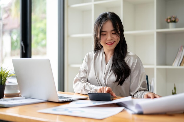 Une belle femme d'affaires asiatique utilise une calculatrice pour calculer les ventes à son bureau au bureau